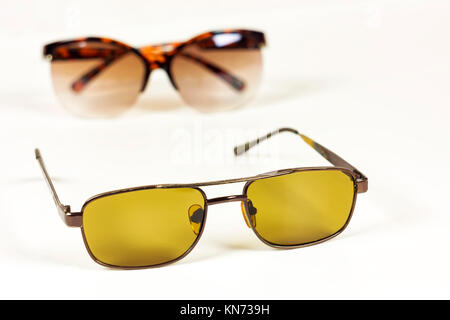 On a white background in the foreground lie men's sunglasses from the sun, in the background lie female glasses from the sun Stock Photo