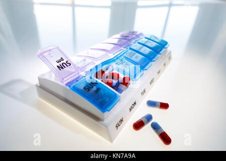 A weekly pill dispenser with one compartment open and full of tablets suggesting over medication Stock Photo