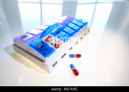 A weekly pill dispenser with one compartment open and full of various tablets suggesting over medication Stock Photo