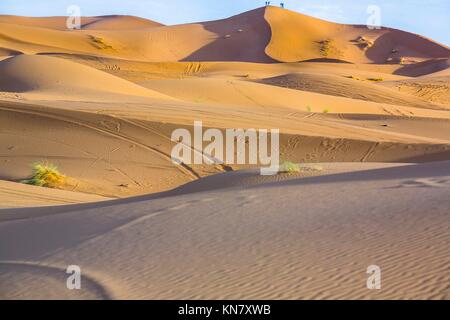 People admire the sunrise from a hill. Several sand hill at Erg Chebbi in the Sahara desert. Ers are large dunes formed by wind-blown sand.