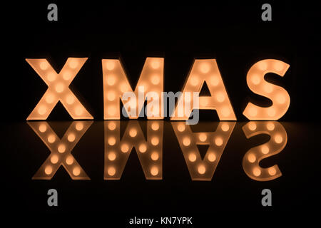 Illuminating Xmas Letters against dark background reflecting on Glass Surface Stock Photo