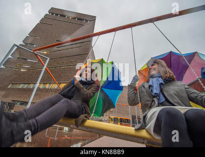 Tate Modern, London, UK. 11 December, 2017. Eleven swings have been installed outside the gallery’s Blavatnik building, as part of a large-scale interactive installation by Danish collective SUPERFLEX. One Two Three Swing! is the first Hyundai Commission to extend beyond the Turbine Hall and into the landscape outside. The large-scale installation features eleven 3 seat swings set against the backdrop of the iconic Tate Modern building with members of the local community enjoying the swings for the first time in pouring rain. Credit: Malcolm Park/Alamy Live News. Stock Photo