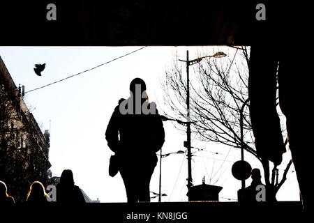 Winter sun silhouettes of people entering the subway street passage and going down stairs, against the city sky witj a flying pigeon Stock Photo