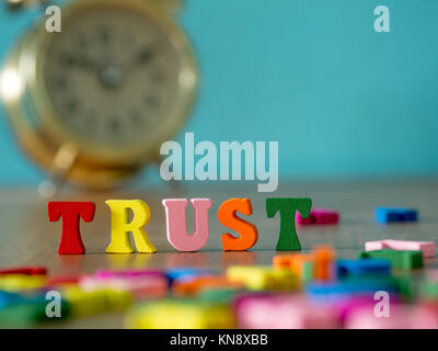 Trust. English alphabet made of wooden letter color. Alphabet trust on wooden table and vintage alarm clock and background is powder blue. Stock Photo