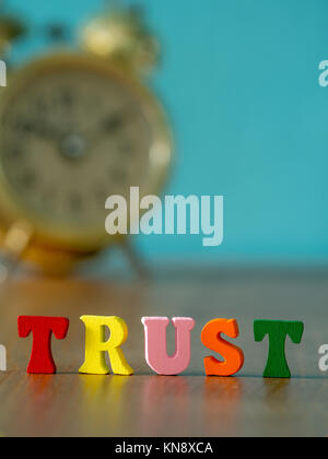 Trust. English alphabet made of wooden letter color. Alphabet trust on wooden table and vintage alarm clock and background is powder blue. Stock Photo