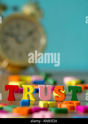 Trust. English alphabet made of wooden letter color. Alphabet trust on wooden table and vintage alarm clock and background is powder blue. Stock Photo