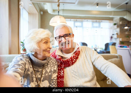 Portrait of happy senior couple holding camera and taking selfie photo on Christmas sitting in cafe Stock Photo