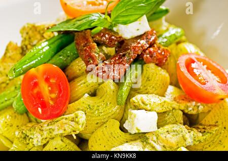 fresh lumaconi pasta and pesto sauce with vegetables and sundried tomatoes,tipycal italian food.