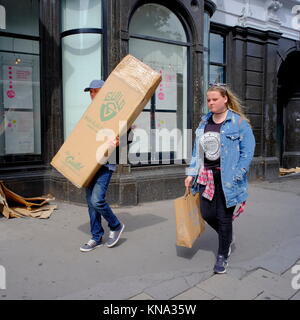 Young man carrying large cardboard  box and young woman carrying brown paper shopping bag in Islington,  London, England, UK Stock Photo