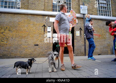 Man with two dogs looking over his shoulder on Brick Lane in Shoreditch, London, England, UK Stock Photo