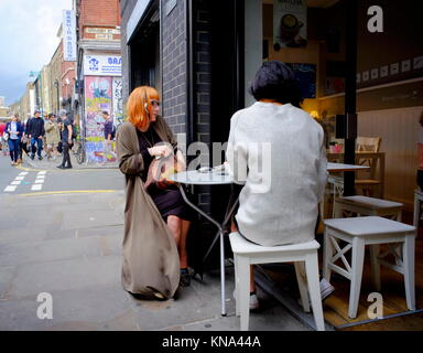 Women sitting at table outside coffee shop on Brick Lane in Shoreditch, London, England, UK Stock Photo
