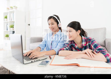 happy elegant woman student wearing headset using e-learning system doing online testing and her classmate looking at mobile computer screen studying  Stock Photo