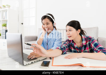 smiling elegant girl student wearing headphone using online e-learning system studying and friend pointing computer screen to assist her finished test Stock Photo