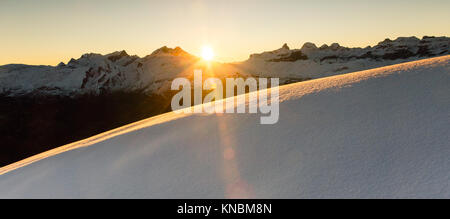 Beautiful sunrise in snowy mountain landscape. Sunbeams illuminating unspoiled powder snow. Alps, Switzerland. Stock Photo
