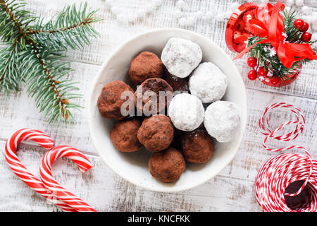 Chocolate truffles in white bowl. Christmas sweets, Christmas chocolate candies, candy cane and fir tree branch on white table. Top view Stock Photo