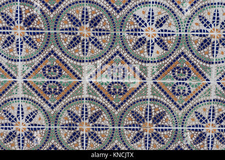 Close up of a colorful mosaic tile wall with orange, green, blue and white tile and brown and white grout. It has a floral motif. Stock Photo