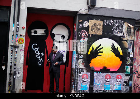 Man smoking while using his mobile phone near Brick Lane in east London Stock Photo