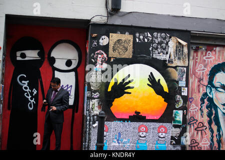 Man smoking while using his mobile phone near Brick Lane in east London Stock Photo