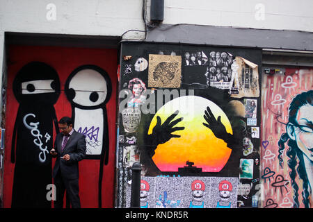 Man smoking while using his mobile phone near Brick Lane in east London Stock Photo