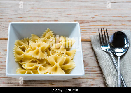 Bowl cooked farfalle pasta with fork and spoon and napkin, serviette. Stock Photo