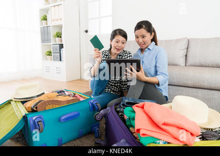 happy beautiful sisters using mobile digital tablet computer booking airplane seat and booking travel schedule through online system at home. Stock Photo