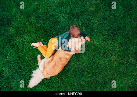 Overhead view of a boy lying on grass hugging his golden retriever dog Stock Photo