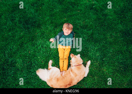 Overhead view of a boy lying on grass playing with his golden retriever dog Stock Photo