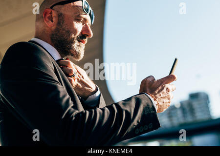 Mature businessman outdoors, using smartphone, low angle view Stock Photo