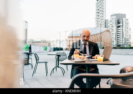 Mature businessman sitting outdoors at cafe, using laptop Stock Photo