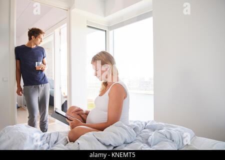 Pregnant young woman cross legged on bed using digital tablet Stock Photo