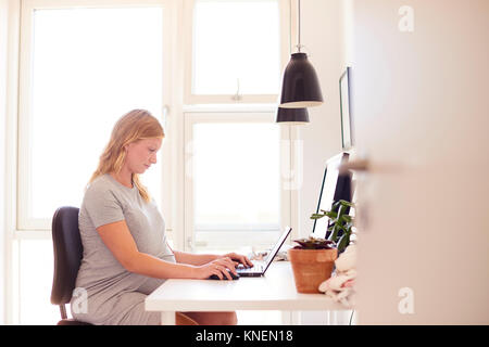Pregnant young woman at desk typing on laptop Stock Photo