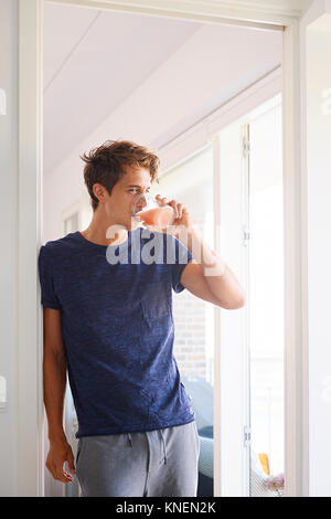 Mid adult man leaning against doorway drinking fruit juice Stock Photo
