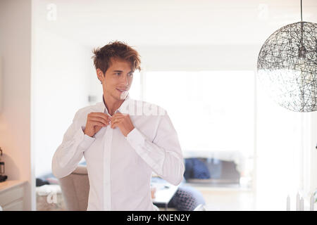 Mid adult man in living room buttoning shirt Stock Photo