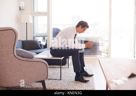 Businessman sitting on coffee table looking at smartphone Stock Photo