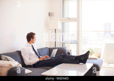 Businessman sitting on sofa using laptop Stock Photo