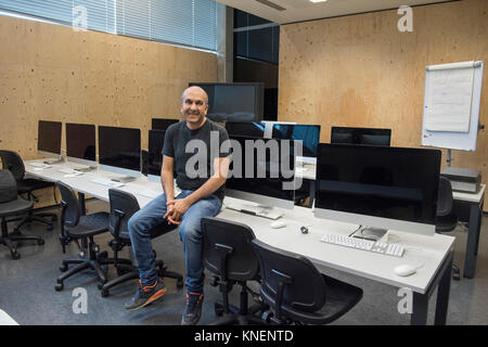 Man sitting on desk in computer room looking at camera smiling Stock Photo