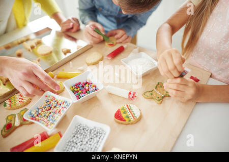 Hands of boy, his sister and mother decorating easter biscuits at kitchen counter Stock Photo
