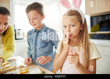 Girl licking her fingers while preparing easter biscuits on kitchen counter Stock Photo