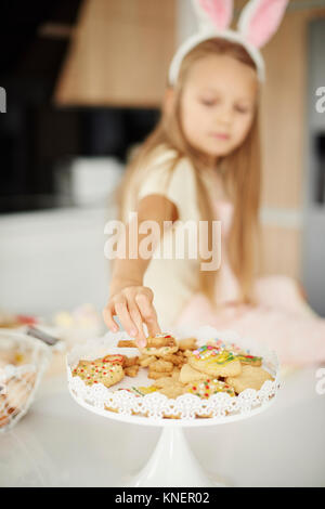 Girl selecting from easter biscuits on kitchen counter Stock Photo