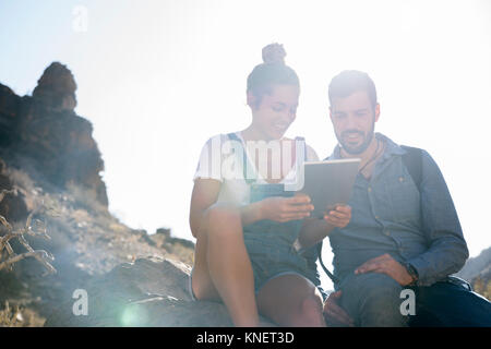 Young hiking couple looking at digital tablet in sunlit valley, Las Palmas, Canary Islands, Spain Stock Photo