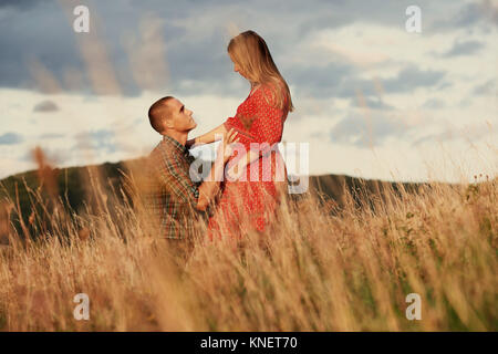 Mid adult man kneeling with hand on pregnant wife's stomach in field Stock Photo