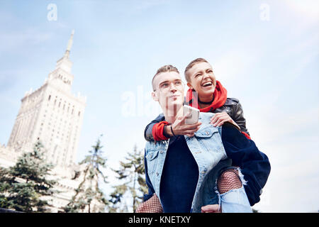 Young man giving laughing girlfriend a piggy back in city Stock Photo