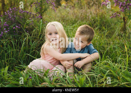 Boy and girl sitting in tall grass together Stock Photo