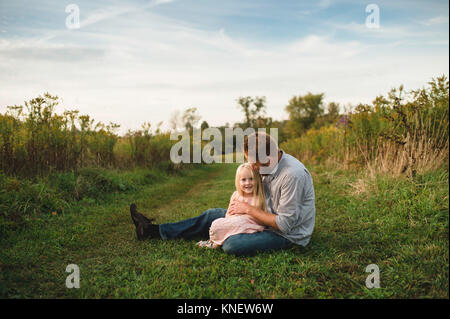 Daughter sitting on fathers lap on grass Stock Photo