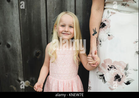 Portrait of girl holding dandelion clock and mother hand looking at camera smiling Stock Photo