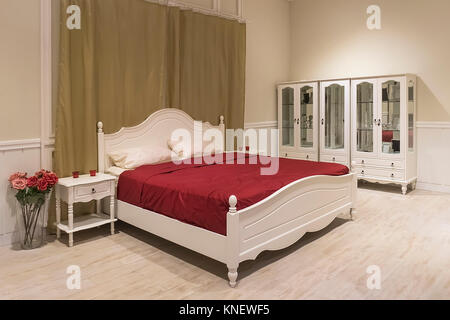 White wooden bed with dark red blanket and white pillows. Stock Photo