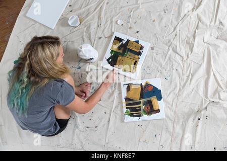 Overhead view of female artist crouching on dust sheet painting abstract canvas Stock Photo
