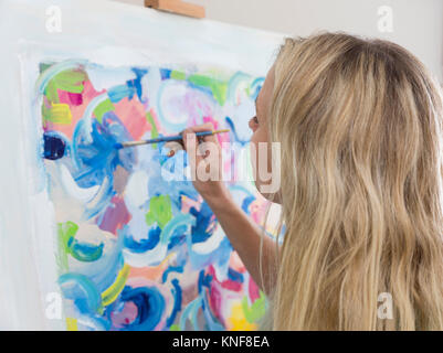 Over shoulder view of female artist painting abstract canvas  in studio Stock Photo