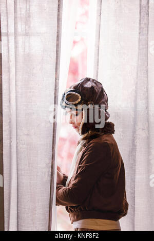 Girl looking out through window wearing pilot costume for halloween Stock Photo