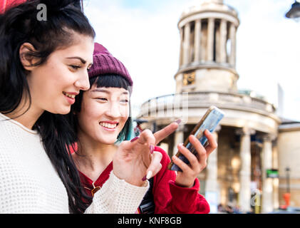 Two young stylish women looking at smartphone, London, UK Stock Photo